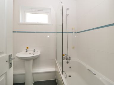 A bathroom with a pedestal sink and a bathtub with a shower and glass screen at Harcombe House Bungalow 4 in Chudleigh