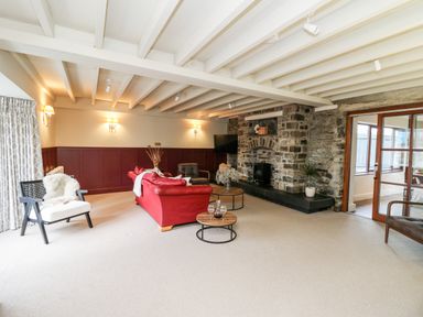 A living room with a red sofa two round wooden coffee tables a stone fireplace and wooden framed glass doors at Dant Y Llew in Bow Street Wales