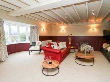 A living room with a red leather sofa wooden tables and a bay window at Dant Y Llew in Bow Street Wales
