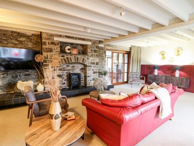 A living room with a red sofa a wooden coffee table a stone fireplace and a mounted tv at Dant Y Llew in Bow Street Wales