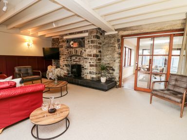 A living room with stone wall fireplace wooden tables and chairs at Dant Y Llew in Bow Street Wales