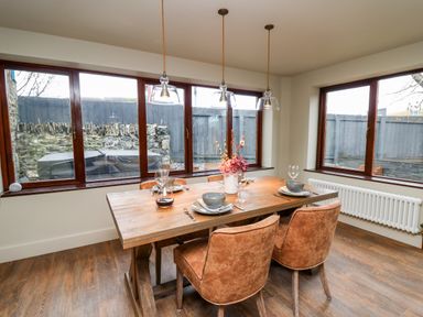 A dining room with a wooden table set for four and three pendant lights over the table at Dant Y Llew in Bow Street Wales