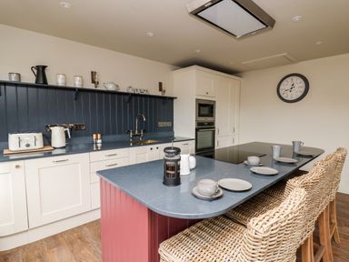 A kitchen with a blue countertop island and wicker chairs at Dant Y Llew in Bow Street Wales