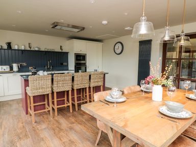 A kitchen and dining area with wicker bar stools and a wooden dining table at Dant Y Llew in Bow Street Wales