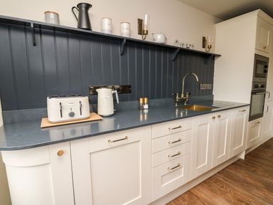 A kitchen with white cabinets a gray countertop a toaster kettle sink and wall shelf at Dant Y Llew in Bow Street Wales