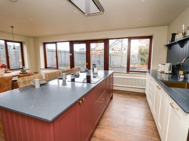 A kitchen with a large island with cups and plates a dining table and chairs beside windows at Dant Y Llew in Bow Street Wales