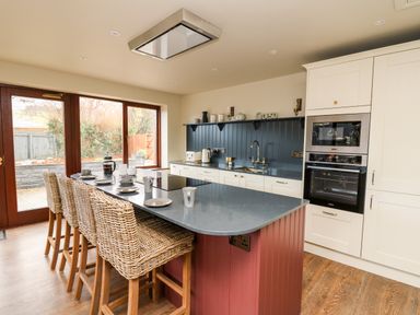 A kitchen with an island and wicker bar stools next to large windows at Dant Y Llew in Bow Street Wales