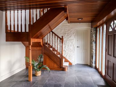 An entryway with wooden stairs stone wall tiled floor and wooden door at Dant Y Llew in Bow Street Wales