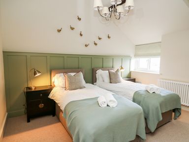 A bedroom with two single beds green bed throws and bedside tables with lamps at Dant Y Llew in Bow Street Wales