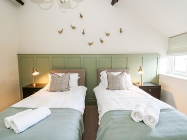 A bedroom with two single beds side by side each with a pillow and rolled towels on green bed covers and bedside tables with lamps at Dant Y Llew in Bow Street Wales