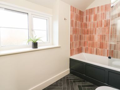 A bathroom with a bathtub with orange wall tiles a window with a plant on the sill and black herringbone floor tiles at Dant Y Llew in Bow Street Wales