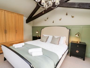 A bedroom with a bed flanked by two bedside tables with lamps and a wooden wardrobe in the corner at Dant Y Llew in Bow Street Wales