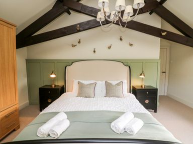 A bedroom with a bed with pillows and rolled towels bedside tables with lamps and decorated wall at Dant Y Llew in Bow Street Wales