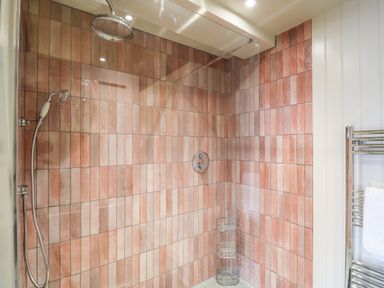 A shower area with pink tiles a rainfall shower head a handheld shower and a chrome towel rack with a towel at Dant Y Llew in Bow Street Wales