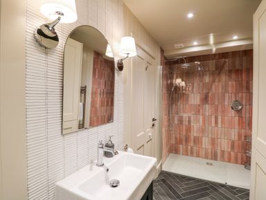 A bathroom with a white sink and mirror and a walk in shower with reddish tiles at Dant Y Llew in Bow Street Wales