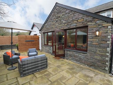 An outdoor patio area with stone paving a wicker sofa and chairs with cushions an umbrella and a stone wall house with windows and a door at Dant Y Llew in Bow Street Wales