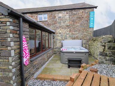 An outdoor patio area with a hot tub against a stone wall and a pink and white towel hanging on a hook at Dant Y Llew in Bow Street Wales
