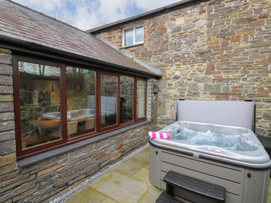 An outdoor patio area with a hot tub next to a stone wall and window at Dant Y Llew in Bow Street Wales