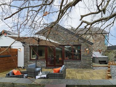 A stone exterior house with patio furniture and an umbrella and a hot tub at Dant Y Llew in Bow Street Wales