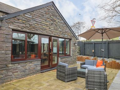 An outdoor patio with stone walls wicker furniture and a large umbrella at Dant Y Llew in Bow Street Wales