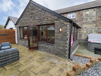 A stone house with an open glass door leading to a patio with outdoor furniture and a hot tub at Dant Y Llew in Bow Street Wales