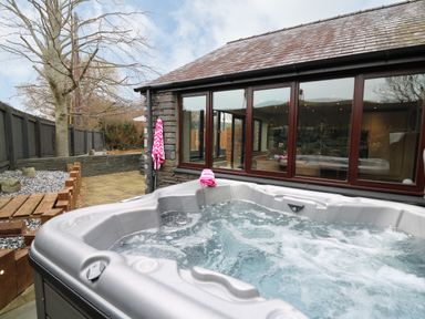 An outdoor hot tub next to a stone building with large windows at Dant Y Llew in Bow Street Wales