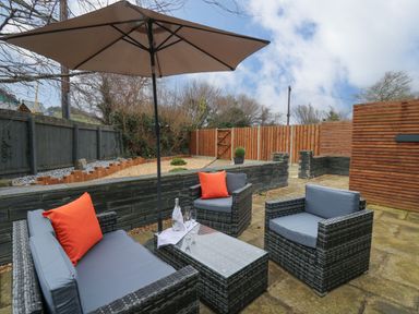 An outdoor patio area with wicker furniture including a sofa and two armchairs with orange cushions and a large umbrella over a table at Dant Y Llew in Bow Street Wales