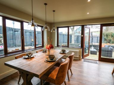 A dining room with a wooden table set with plates bowls and wine glasses next to large windows and glass doors at Dant Y Llew in Bow Street Wales