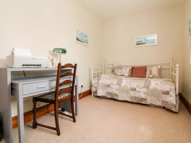 A small room with a desk, chair, and a daybed with floral bedding at Home Farm Cottage in Fremington Devon