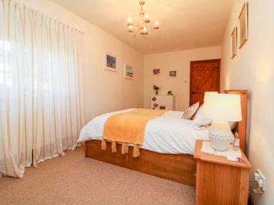 A bedroom with a wooden bed a bedside table with lamp a chest of drawers and a wooden door at Home Farm Cottage in Fremington Devon