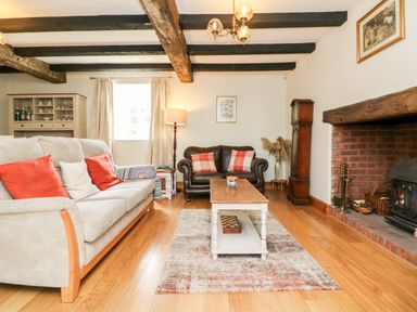 A living room with a sofa and armchair near a fireplace and wooden beams on the ceiling at Home Farm Cottage in Fremington Devon