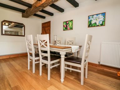 A dining room with a wooden table and six chairs under exposed ceiling beams at Home Farm Cottage in Fremington Devon