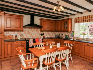 A kitchen with wooden cabinets a dining table with six chairs and a window with striped blinds at Home Farm Cottage in Fremington Devon