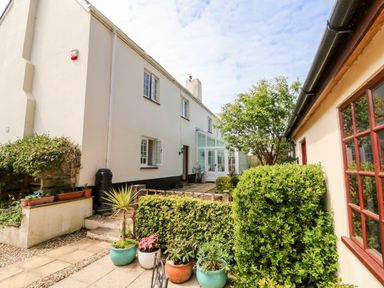 A garden area with potted plants and shrubs between two buildings with windows at Home Farm Cottage in Fremington Devon