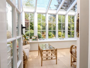 A sunroom with wicker chairs and a glass coffee table overlooking a garden at Home Farm Cottage in Fremington Devon