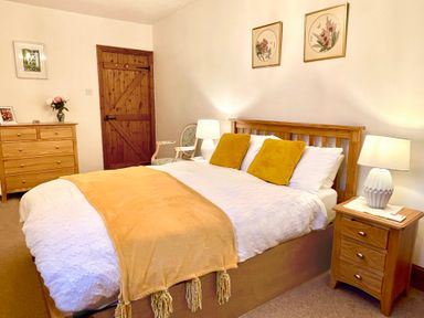 A bedroom with a wooden bed with yellow pillows and blanket a wooden chest of drawers a wooden door and two lamps at Home Farm Cottage in Fremington Devon