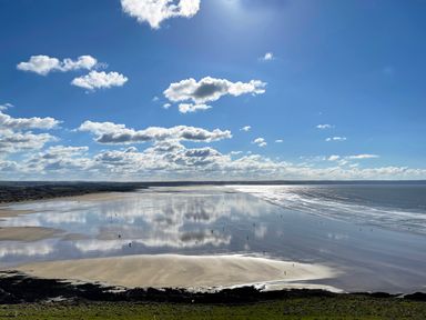 A wide beach with wet sand reflecting clouds under a blue sky at Home Farm Cottage in Fremington Devon