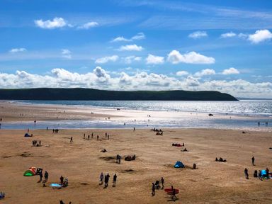 A sandy beach with people walking and sitting near the water and hills in the background at Home Farm Cottage in Fremington Devon