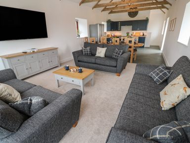 A living room with three gray sofas a wooden coffee table and a dining area with wooden chairs and blue cabinets at Pol View Gunwalloe near Helston