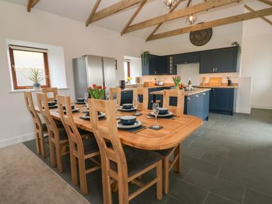 A kitchen and dining area with a wooden dining table set for eight and blue cabinets at Pol View in Gunwalloe near Helston
