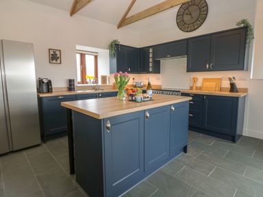 A kitchen with blue cabinets wooden countertops kitchen island and stainless steel refrigerator at Pol View in Gunwalloe near Helston