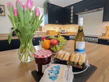 A kitchen countertop with a vase of pink tulips a bowl of mixed fruit a bottle of white wine jam clotted cream and scones at Pol View in Gunwalloe near Helston