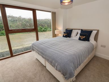 A bedroom with a bed covered with a patterned blanket and pillows next to a large window at Pol View in Gunwalloe near Helston