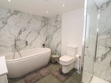 A bathroom with a bathtub, toilet, shower enclosure, and marble walls at Pol View in Gunwalloe near Helston