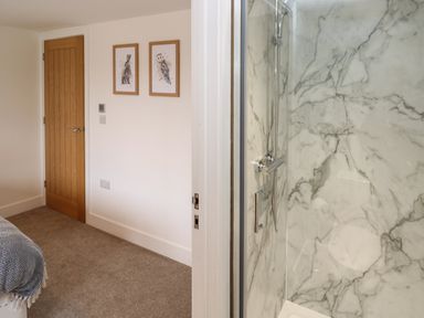 A bedroom with a wooden door and framed animal pictures next to a bathroom with a marble shower at Pol View in Gunwalloe near Helston