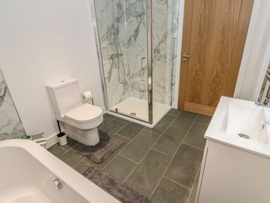 A bathroom with a bathtub toilet shower cubicle sink and wooden door at Pol View in Gunwalloe near Helston