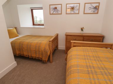 A bedroom with two single beds covered with yellow plaid blankets a wooden dresser with a small flower vase and three framed flower pictures on the wall at Pol View in Gunwalloe near Helston