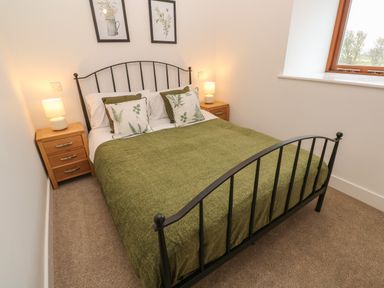 A bedroom with a double bed with green bedding and botanical pillows with wooden nightstands and lamps on each side at Pol View in Gunwalloe near Helston