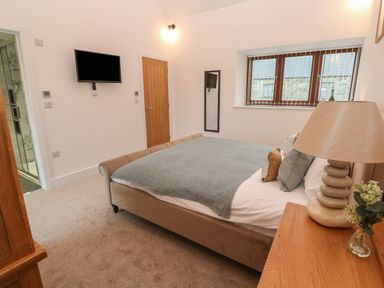A bedroom with a bed a bedside lamp a wall-mounted television a wooden door and a window at Pol View in Gunwalloe near Helston
