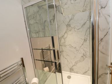 A shower enclosure with marble walls a glass door and a chrome towel rack at Pol View in Gunwalloe near Helston